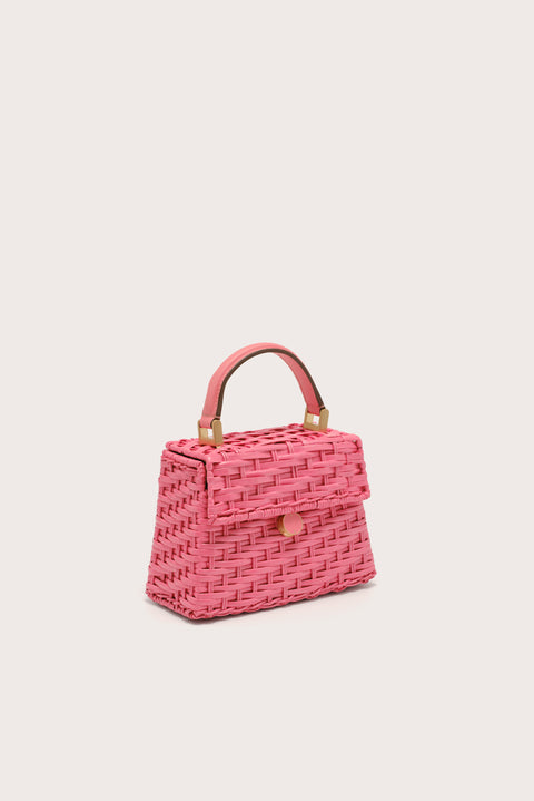Side angle of a pink wicker, trapezoidal handbag that features a top handle and flap closure, complete with gold-toned hardware.