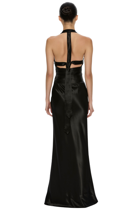 A model viewed from the back wearing a black satin halter-neck maxi dress with a cutout back design, set against a plain white background.