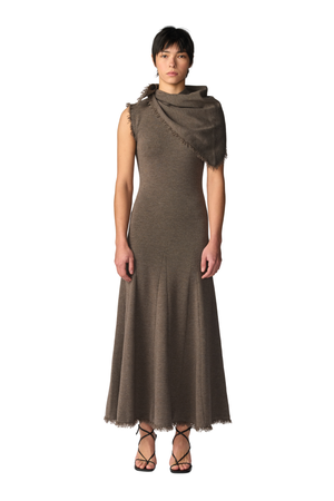 A model wearing a sleeveless maxi dress in a taupe-brown color, styled with a matching fringed shawl draped over one shoulder, set against a plain white background.