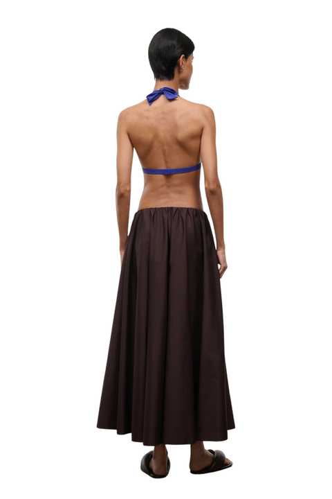 A woman shown from the back wearing a dark brown maxi skirt and a blue halter-style top, standing against a plain white background.