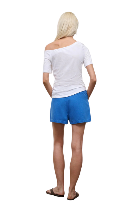A woman shown from the back wearing a white off-the-shoulder short-sleeve top and bright blue shorts, standing against a plain white background.