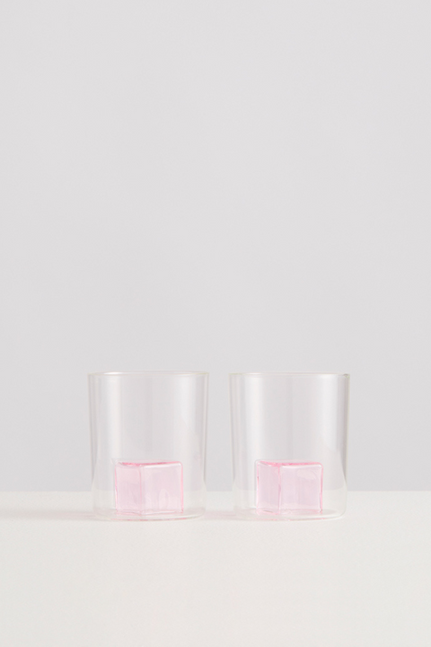 Two clear glasses with pink glass ice cubes inside on a white background