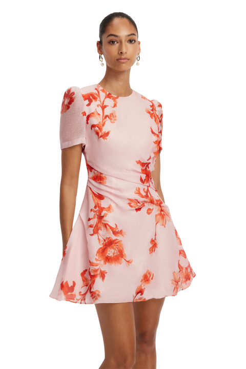 A woman modeling a short-sleeve pink dress with a red-orange floral print, photographed against a plain white studio background.