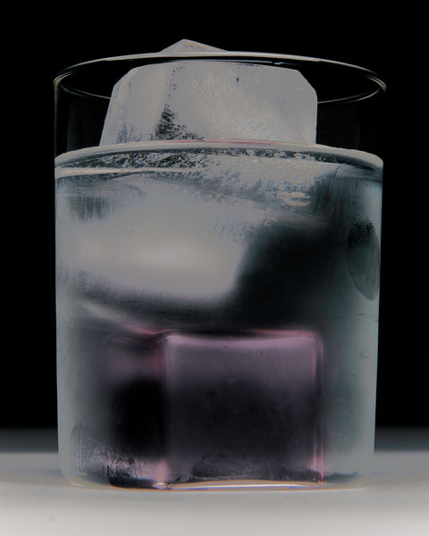 Up close of glass filled with ice water and pink glass ice cube.