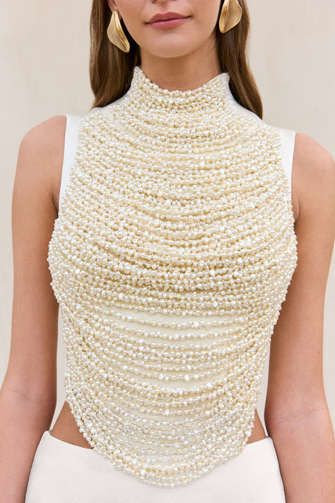 Detail shot of a woman wearing a white tank top that features rows of pearl-beaded strings draped across the bodice.