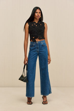 Woman wearing a black sleeveless crop top that is made of crochet floral appliques.