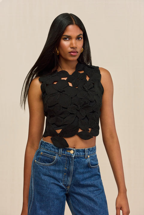 Close up of a woman wearing a black sleeveless crop top that is made of crochet floral appliques.