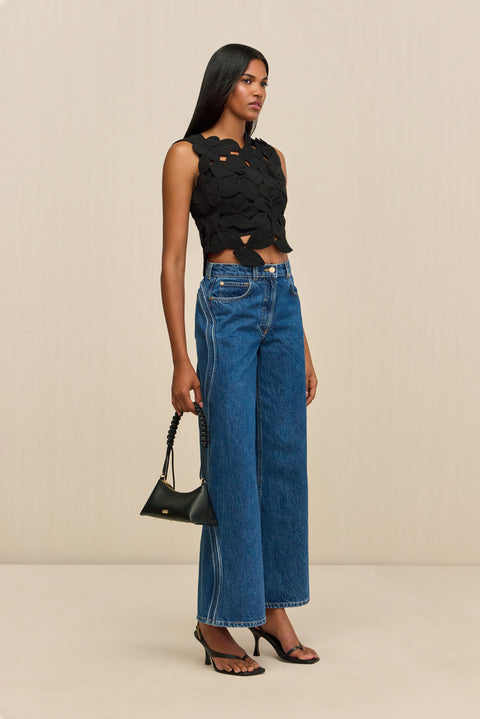 Side-facing woman wearing a black sleeveless crop top that is made of crochet floral appliques.