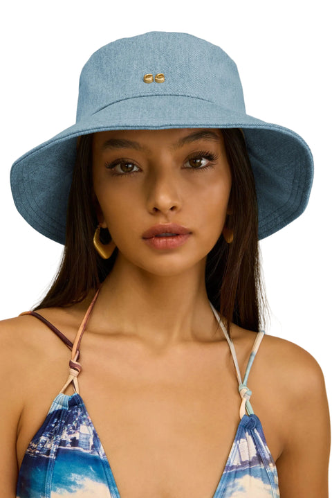 Woman wearing a blue bucket hat and a blue bikini top with white straps against a beige background