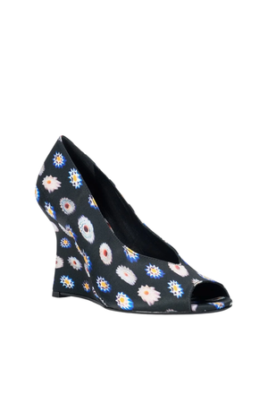 A single women's wedge pump with an open toe, featuring a black base covered in a colorful daisy floral pattern, shown against a plain white background.