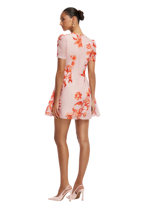 A woman modeling a short-sleeve pink dress with a vibrant orange floral print, shown from a rear three-quarter angle against a solid white background.