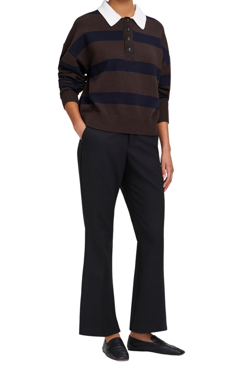 A model wearing a brown and navy striped knit polo sweater with a white collar, paired with black trousers and black loafers, shown against a plain white background.