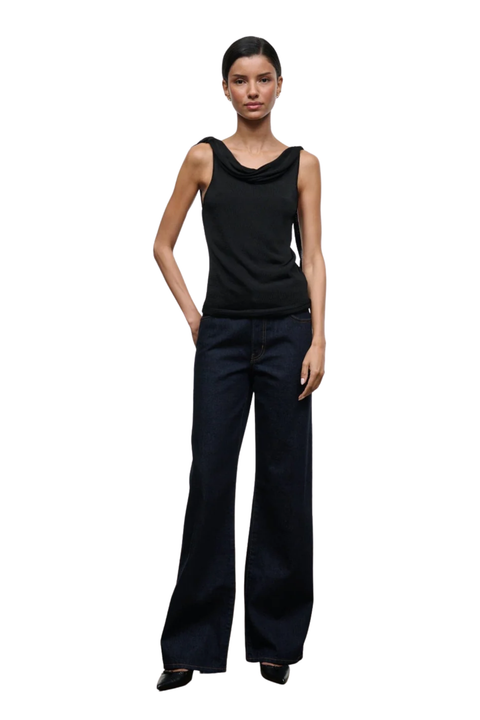 A model wearing a black sleeveless cowl-neck top and dark blue wide-leg trousers, standing against a plain white background.