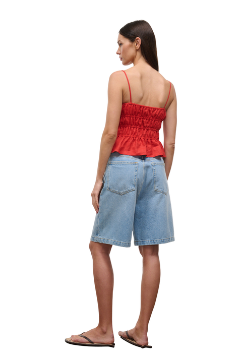 A woman shown from the back wearing a red ruched spaghetti-strap top, light-wash denim shorts, and black flip-flops against a plain white background.