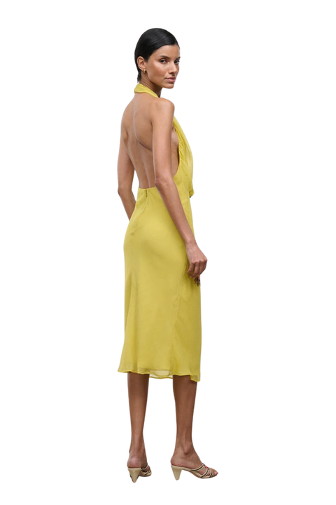 A woman modeling a bright yellow halter-neck midi dress with an open back, shown from a side-rear angle against a plain white background.