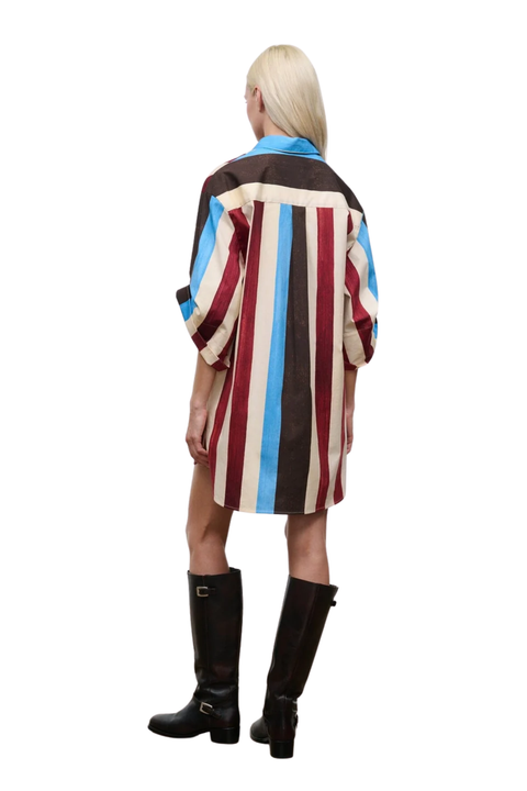 A model shown from the back wearing a short striped dress with vertical stripes in brown, cream, red, and light blue, paired with black knee-high boots against a white background.