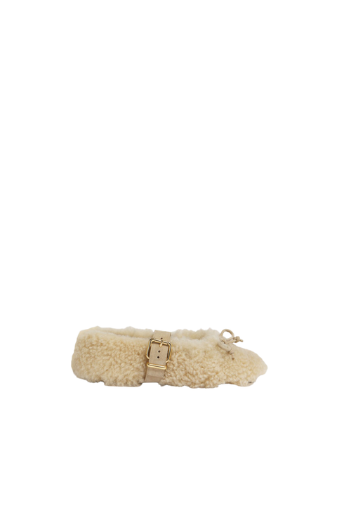 A single beige shearling ballerina flat shoe with a gold buckle strap and a small gold bow detail, shown against a plain white background.