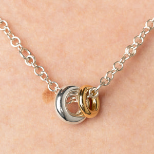 Close up of a woman wearing a Spinelli Kilcollin Gravity necklace with a sterling silver chain and a sterling silver annulet and a smaller yellow gold annulet.