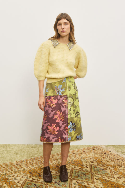 Woman wearing a yellow sweater with short, puff sleeves and an embellished collar, paired with a patterned skirt.