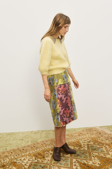 Side-facing woman wearing a yellow sweater with short, puff sleeves and an embellished collar, paired with a patterned skirt.