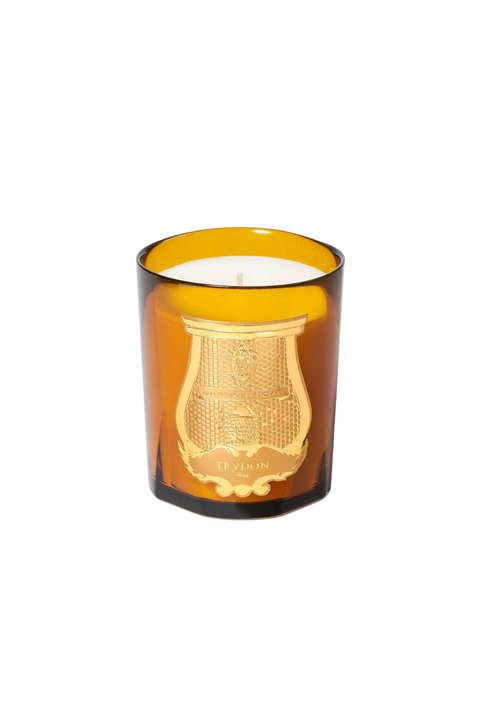 An amber murano glass jar candle with a gold crest emblem on the front, containing white wax, set against a plain white background.
