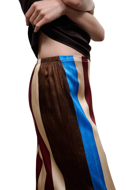 A close-up of a model wearing pants with vertical stripes of dark brown, beige, burgundy, and bright blue.