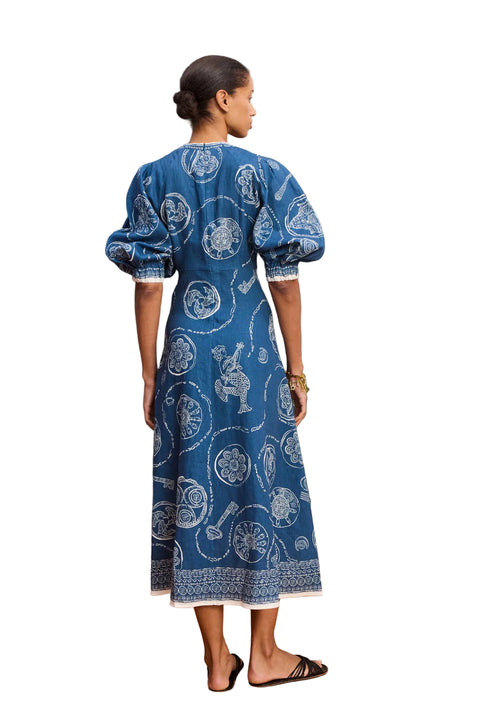 Woman facing away wearing a blue patterned midi dress standing on a white background.