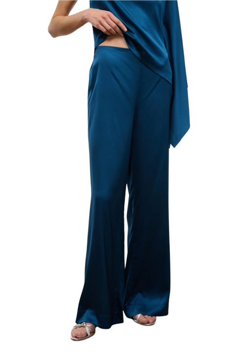 A model wearing a teal blue satin two-piece set consisting of wide-leg pants and an asymmetrical draped top, shown against a plain white background.