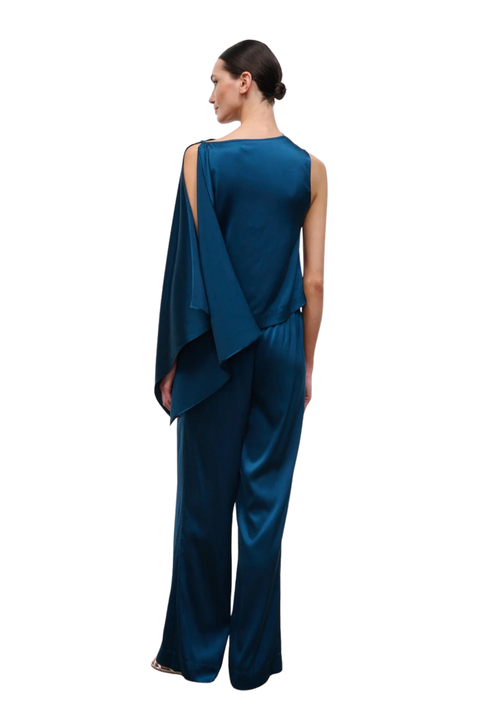 A woman shown from the back wearing a dark teal satin top with draped sleeves and wide-leg pants, photographed against a plain white background.
