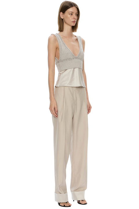 A model wearing a sleeveless beige jumpsuit with a textured ribbed bodice and wide-leg trousers, paired with black sandals, on a solid white background.