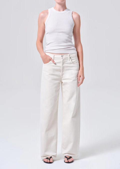 Person wearing white wide-leg, mid-rise jeans and a white top on a white background with hand in front pocket