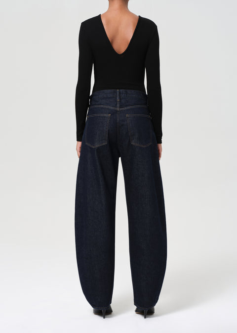Person wearing a black long-sleeve top and dark blue, wide-leg jeans on a white background back view