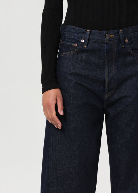 Person wearing a black long-sleeve top and dark blue, wide-leg jeans on a white background zoomed in