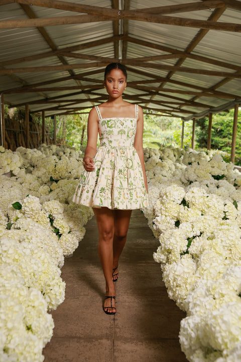 Model walks runway lined with white flowers in tropical print mini dress.