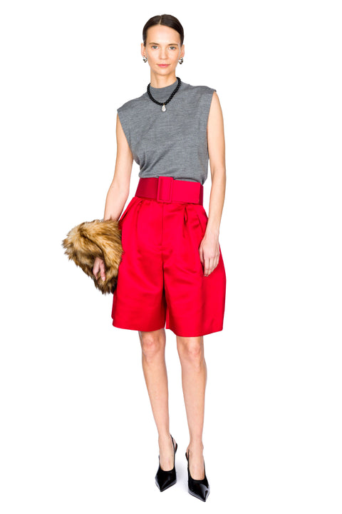 Woman wearing a gray sleeveless top and red wide shorts holding a fur bag on a white background