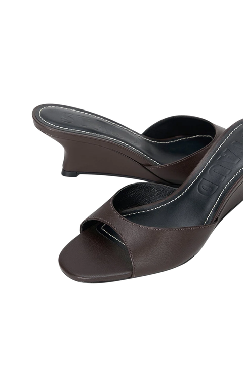 A pair of dark brown leather mule sandals with wedge heels, shown from a high-angle view on a plain white background.