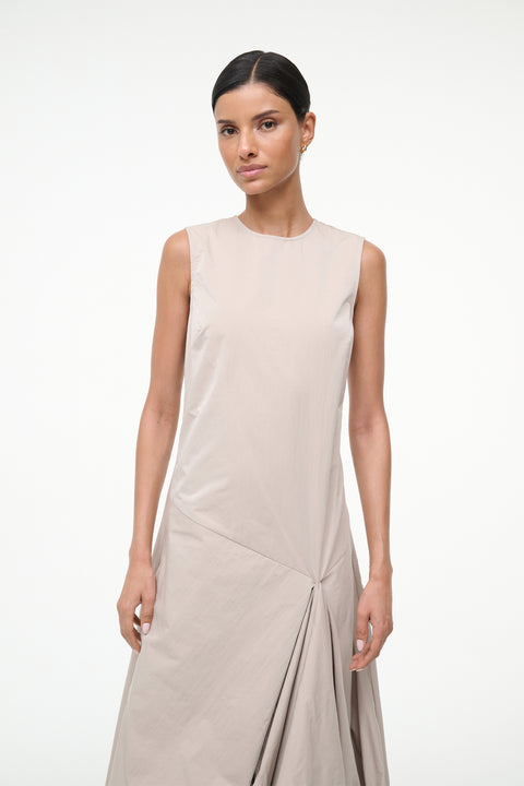Close up of a woman wearing a beige asymmetrical sleeveless maxi dress.