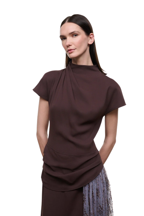 A woman modeling a dark brown short-sleeve top with a gathered, draped neckline and a matching dark brown skirt, set against a plain white background.