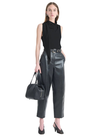 Woman wearing a black sleeveless top and leather pants holding a black handbag on a white background