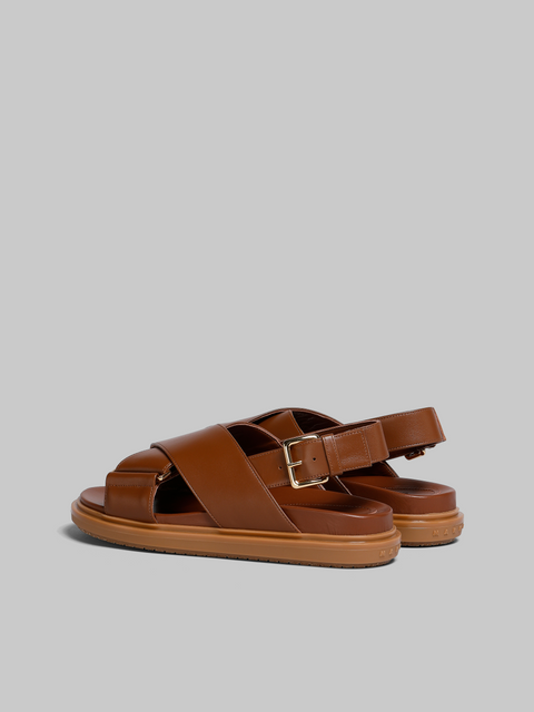 Side view of a pair of brown leather sandals with heel strap and gold hardware.