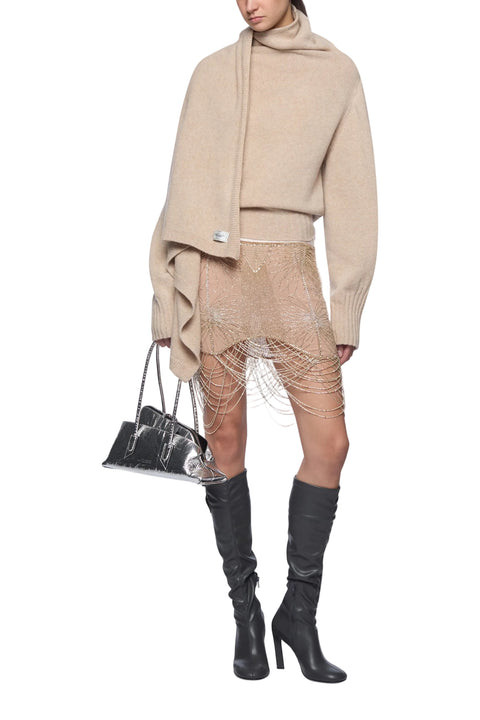 Person wearing a beige sweater, skirt, and knee-high boots holding a black handbag on a white background