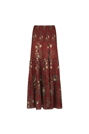 A tiered maxi skirt in a deep burgundy red fabric, decorated with an all-over floral and botanical print in muted green, beige, and gold tones, shown against a plain white background.