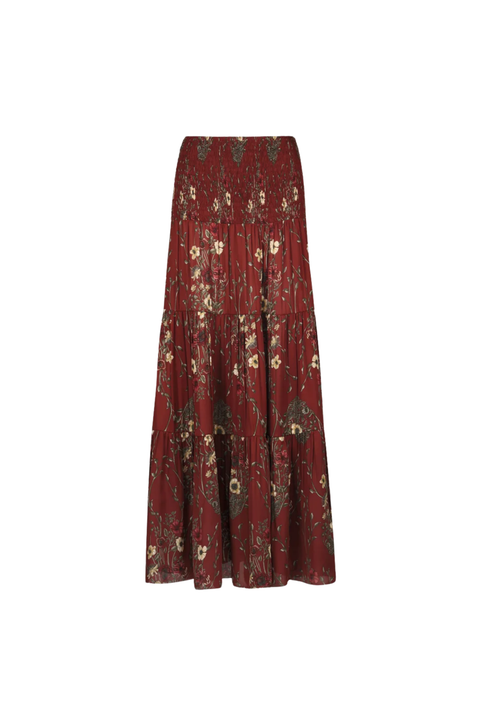 A tiered maxi skirt in a deep burgundy red fabric, decorated with an all-over floral and botanical print in muted green, beige, and gold tones, shown against a plain white background.