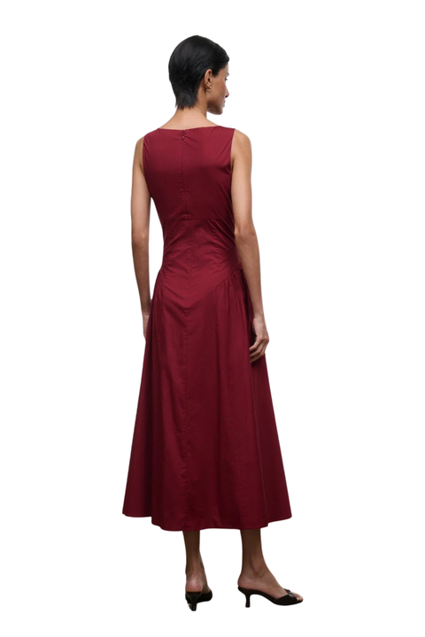 A woman shown from the back wearing a sleeveless, floor-length burgundy dress with a gathered waist, paired with black heeled sandals, against a plain white background.