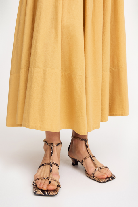 Person wearing yellow midi skirt and snake skin strappy heeled sandals on a white background