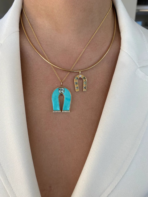 Necklace with a turquoise horseshoe pendant and gold chain on a white background