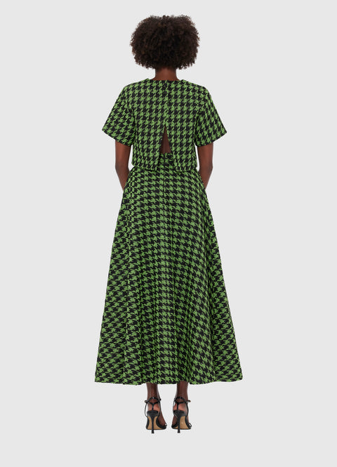 Back view of a woman wearing a green and black houndstooth tweed short sleeve crop top that has an open back and matching A-line maxi skirt, paired with black heels.