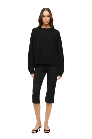A model wearing black capri pants, paired with a black long-sleeve top and black slide sandals, shown against a plain white background.