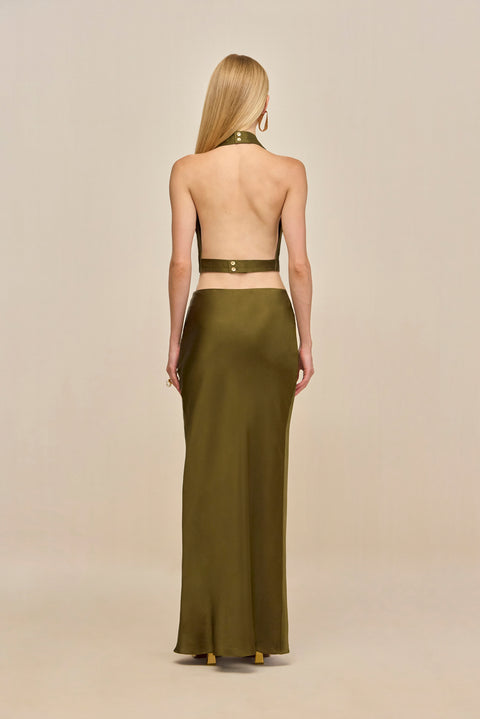 back-facing woman wearing an olive green silk maxi skirt with a matching halter top that has an open back.