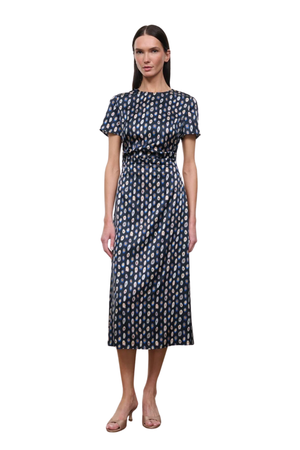 A woman modeling a short-sleeved midi dress with a dark navy blue base and a repeating beige and white geometric pattern, set against a plain white background.